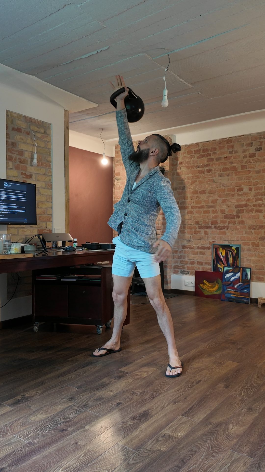 Lee pressing a kettlebell overhead in the studio, headphones on.